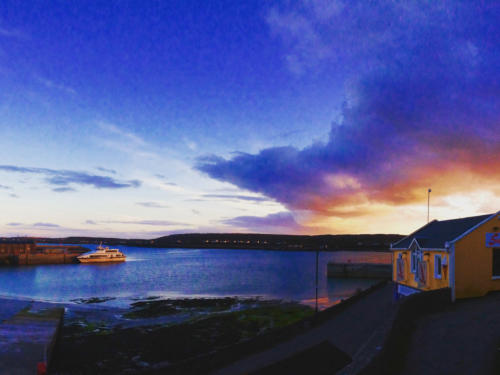 Dusk over the harbour, with a ferry crossing the water and clouds lit orange