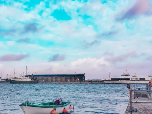 A small boat in the harbour with a ferry and a fishing boat beyond, under a pastel sky