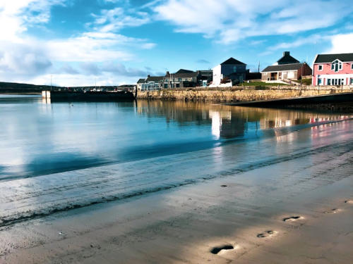 The harbour at low tide, with houses along the shore and the sky reflected in wet sand