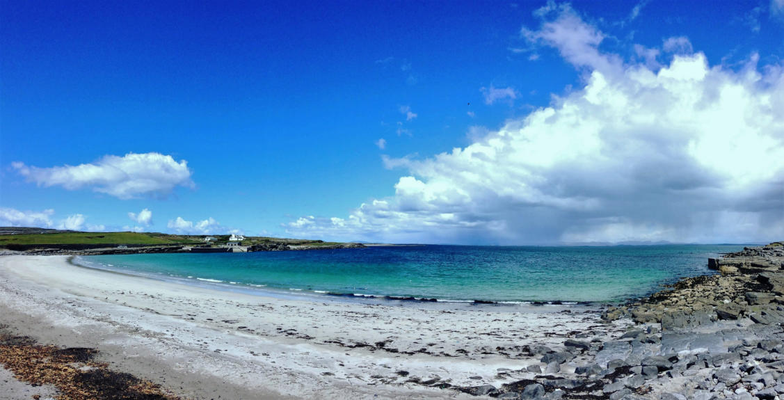 A curving sandy beach and turquoise bay under a deep blue sky with towering white clouds
