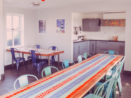 The hostel's dining room and kitchen, with a long mosaic-topped table and brightly coloured chairs