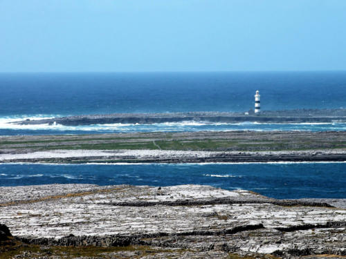 A black-and-white striped lighthouse on a low island across a blue channel